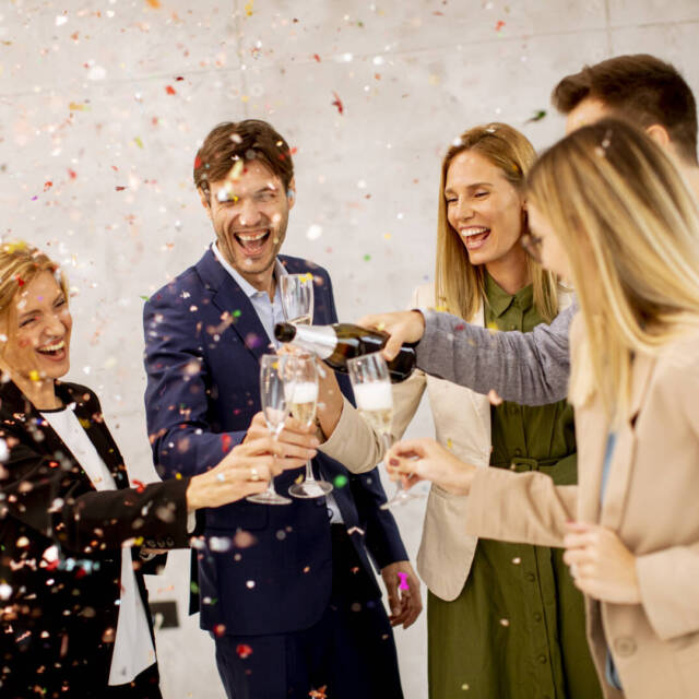 Group of excited business people celebrating and toasting with confetti falling in the office